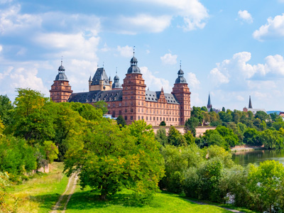 Ein Schloss umgeben von Bäumen und Wasser, mit blauem Himmel und Wolken.