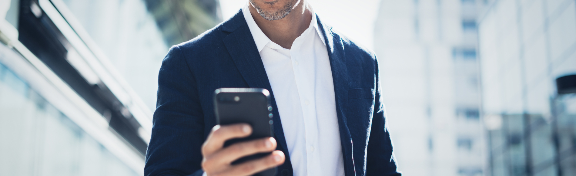Ein Mann in einem Blazer hält ein Smartphone in der Hand, während er in eine Stadtlandschaft blickt.