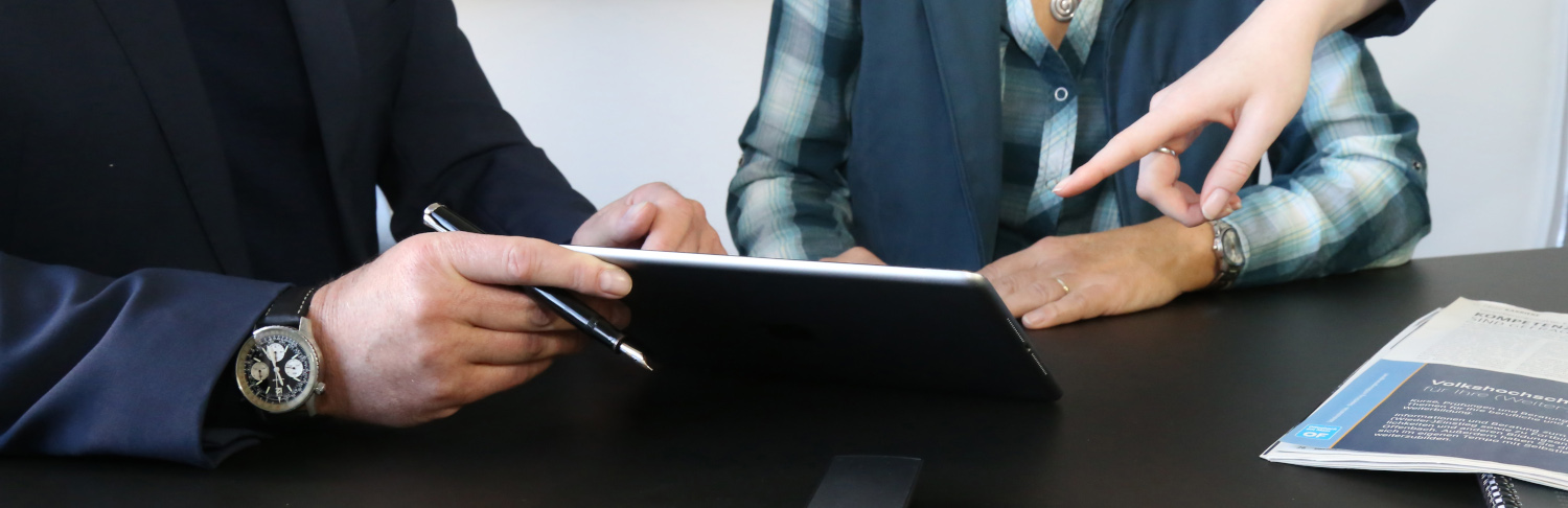 Zwei Personen betrachten ein Tablet, während eine Hand auf den Bildschirm zeigt.
